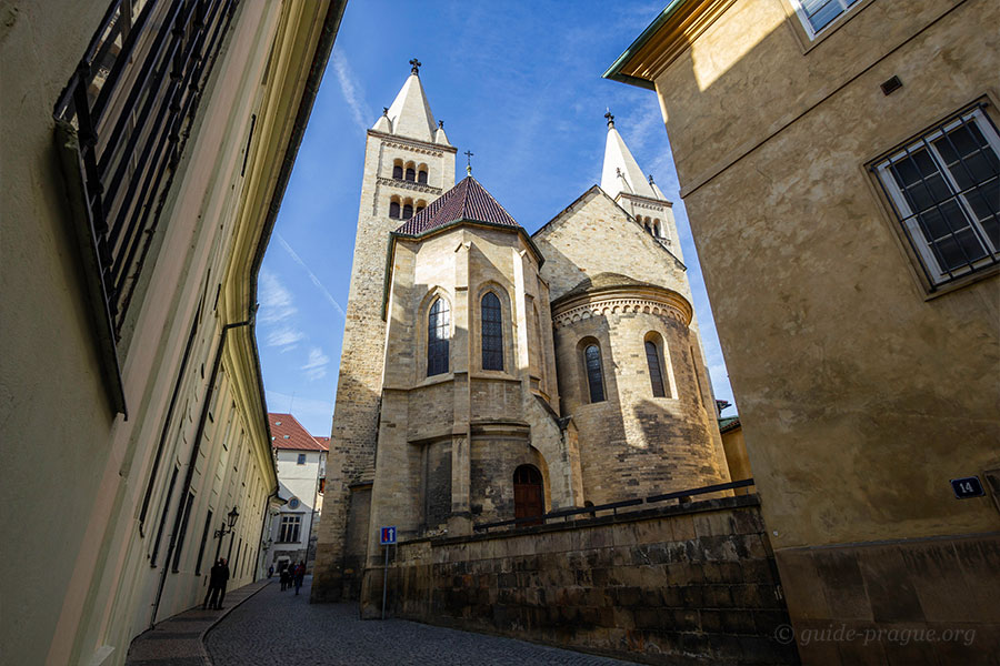 Rear view of St. George's Basilica at Prague Castle, showing its Romanesque architecture between narrow streets.