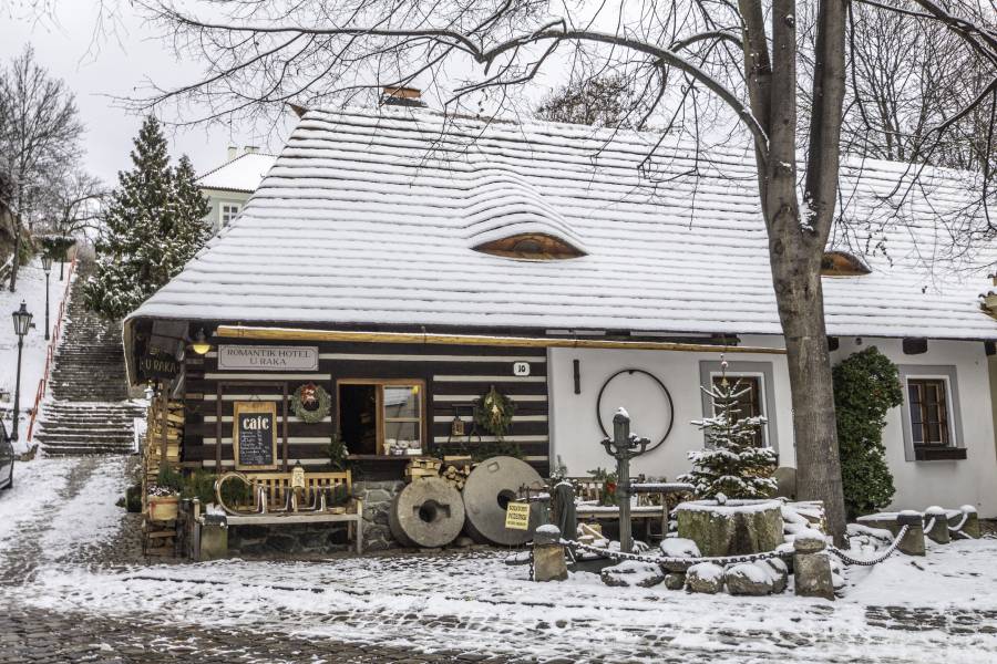 A charming café and historical building surrounded by snow, nestled along a cobblestone path in a quaint area of Prague